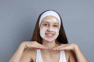 Photo of Teenage girl with cleansing foam on her face against grey background. Acne treatment