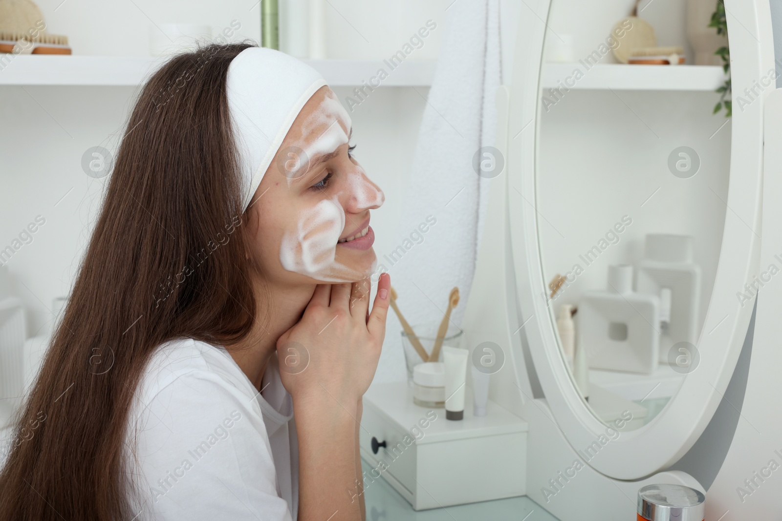 Photo of Teenage girl with cleansing foam on her face near mirror indoors. Acne treatment