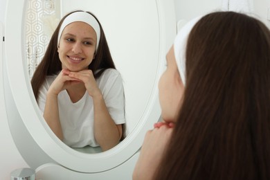 Photo of Teenage girl with acne problem looking in mirror indoors