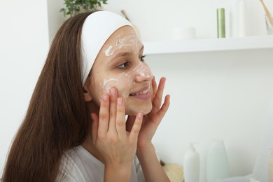 Photo of Teenage girl applying cream onto face at home, space for text. Acne treatment