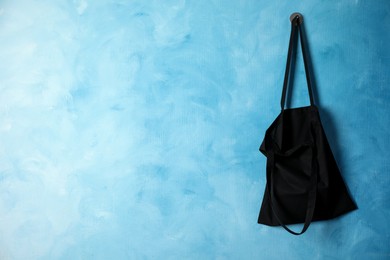 Photo of Black eco bag hanging on light blue wall. Mockup for design