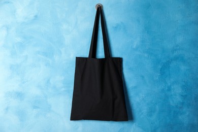 Photo of Black eco bag hanging on light blue wall. Mockup for design