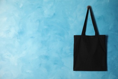 Photo of Black eco bag hanging on light blue wall. Mockup for design