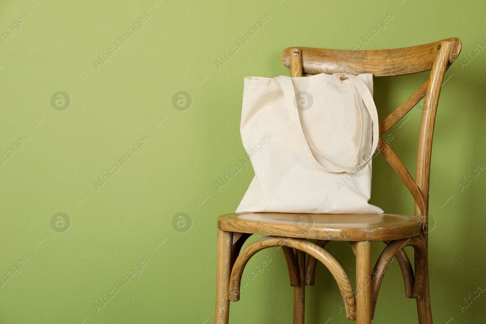 Photo of One eco bag on wooden chair near green wall. Mockup for design