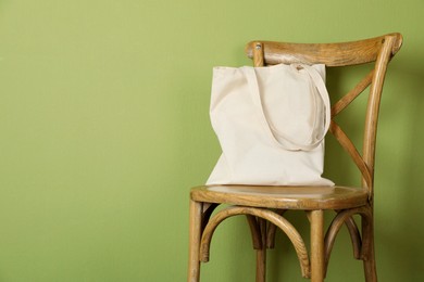 Photo of One eco bag on wooden chair near green wall. Mockup for design