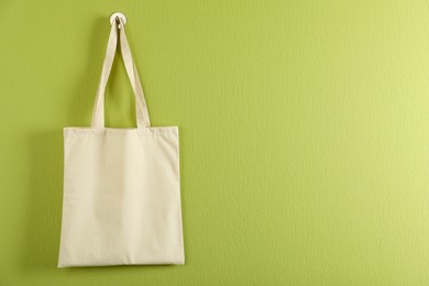 Photo of One eco bag hanging on green wall. Mockup for design