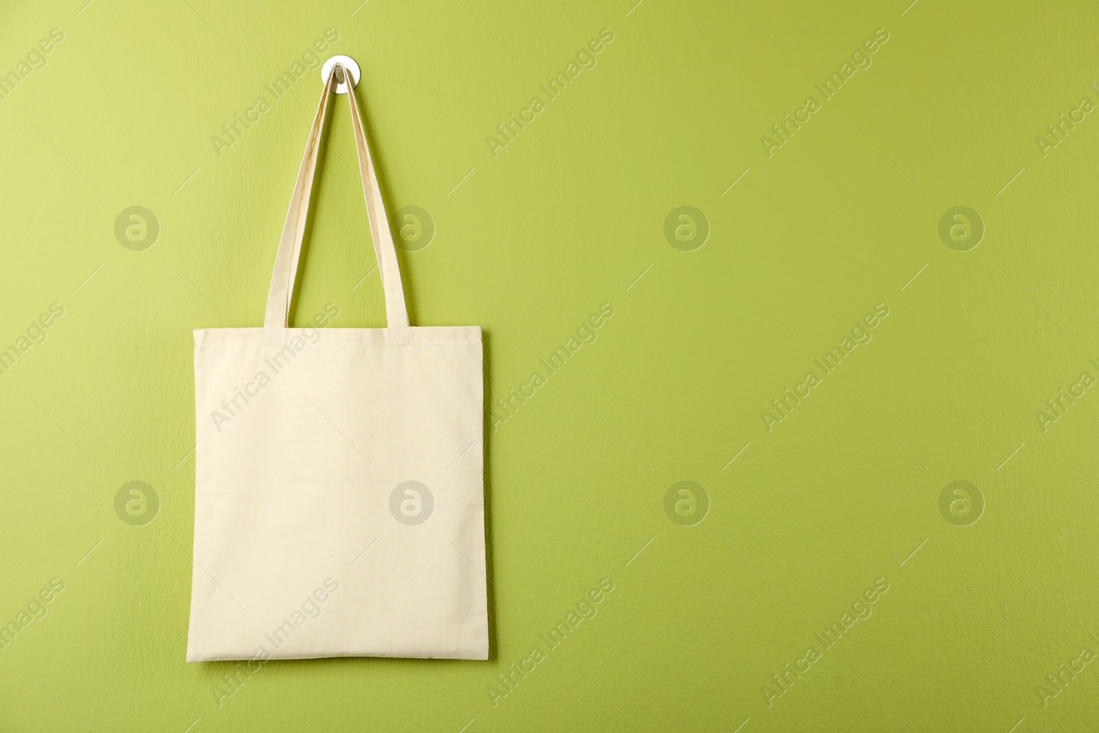 Photo of One eco bag hanging on green wall. Mockup for design