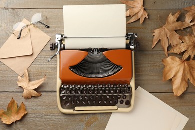 Photo of Vintage typewriter with paper sheet, envelope, glasses and leaves on wooden table, flat lay
