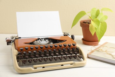 Photo of Vintage typewriter with sheet of paper, glasses, notebook and houseplant on white wooden table