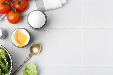 Soft boiled eggs in cups served on white tiled table, space for text