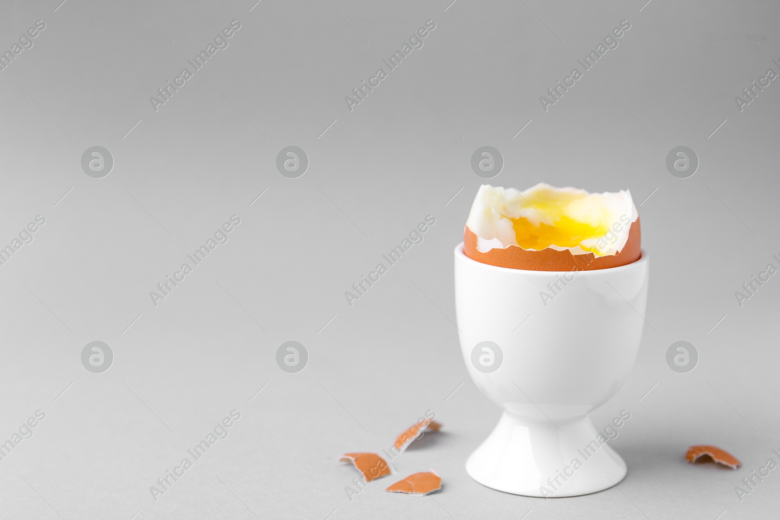 Photo of Soft boiled egg in cup on light grey background, space for text