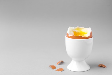 Photo of Soft boiled egg in cup on light grey background, space for text