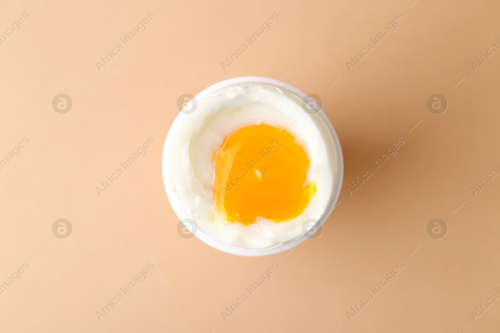 Photo of Soft boiled egg in cup on beige background, top view