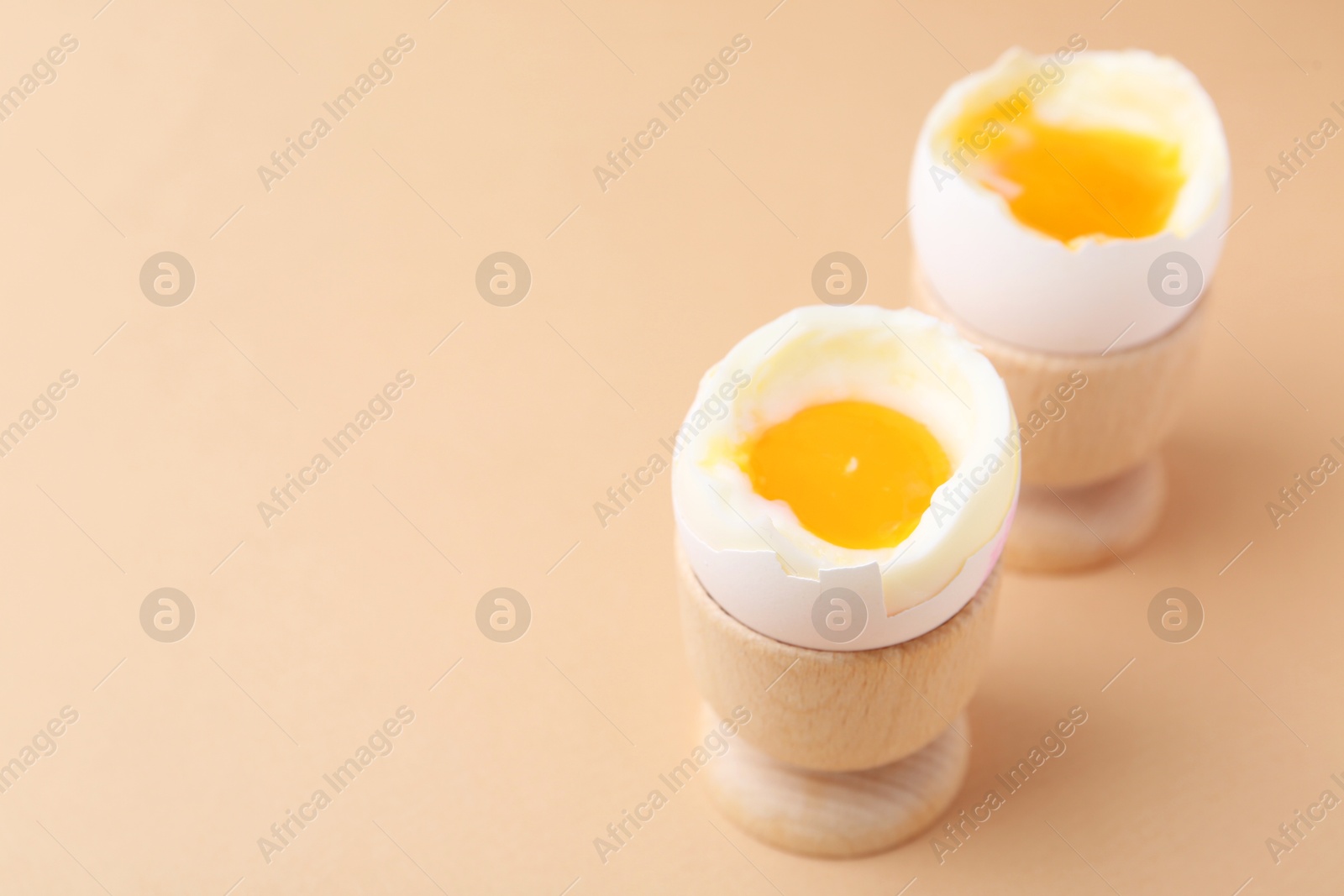 Photo of Soft boiled eggs in cups on beige background, closeup. Space for text