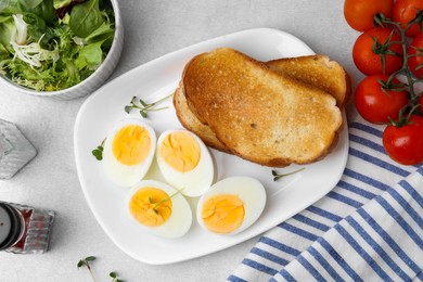 Photo of Hard boiled eggs with bread and tomatoes on light table, flat lay