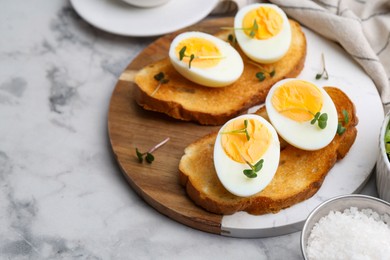 Photo of Sandwiches with hard boiled eggs on white marble table, closeup