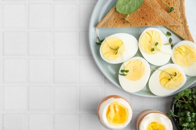 Photo of Cut hard boiled eggs with bread on white tiled table, flat lay. Space for text