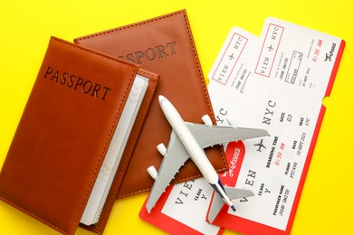 Photo of Travel agency. Flight tickets, passports and plane model on yellow background, flat lay