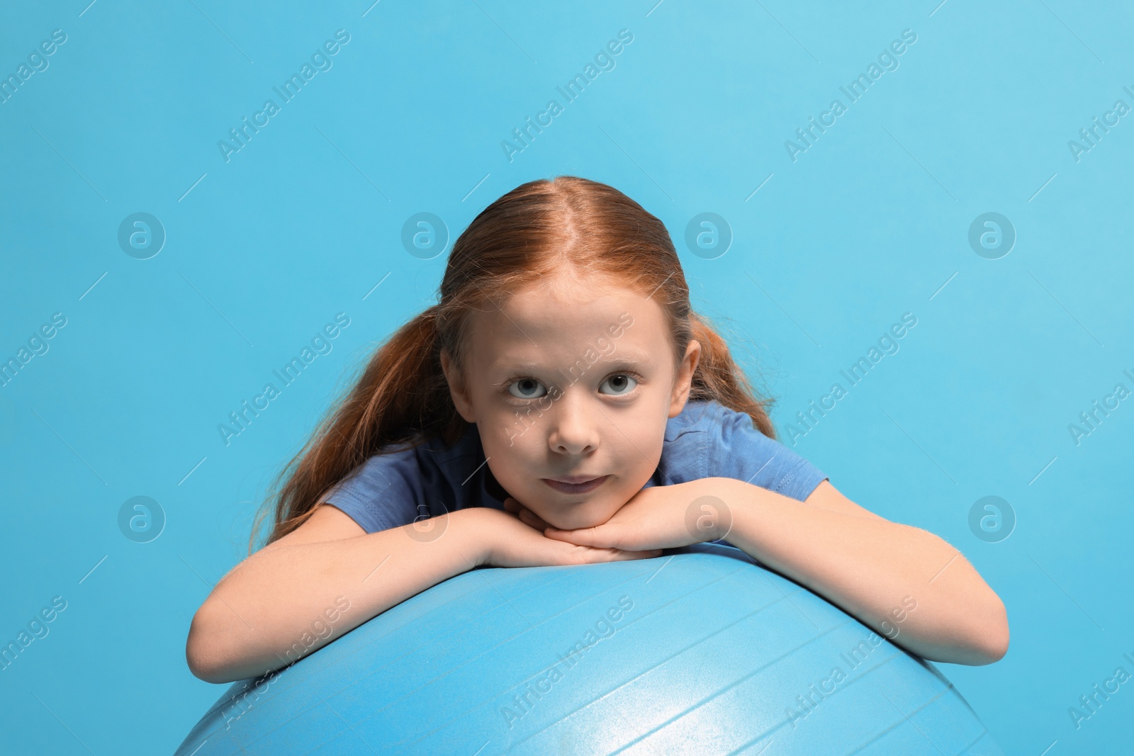 Photo of Cute little girl with fitness ball on light blue background