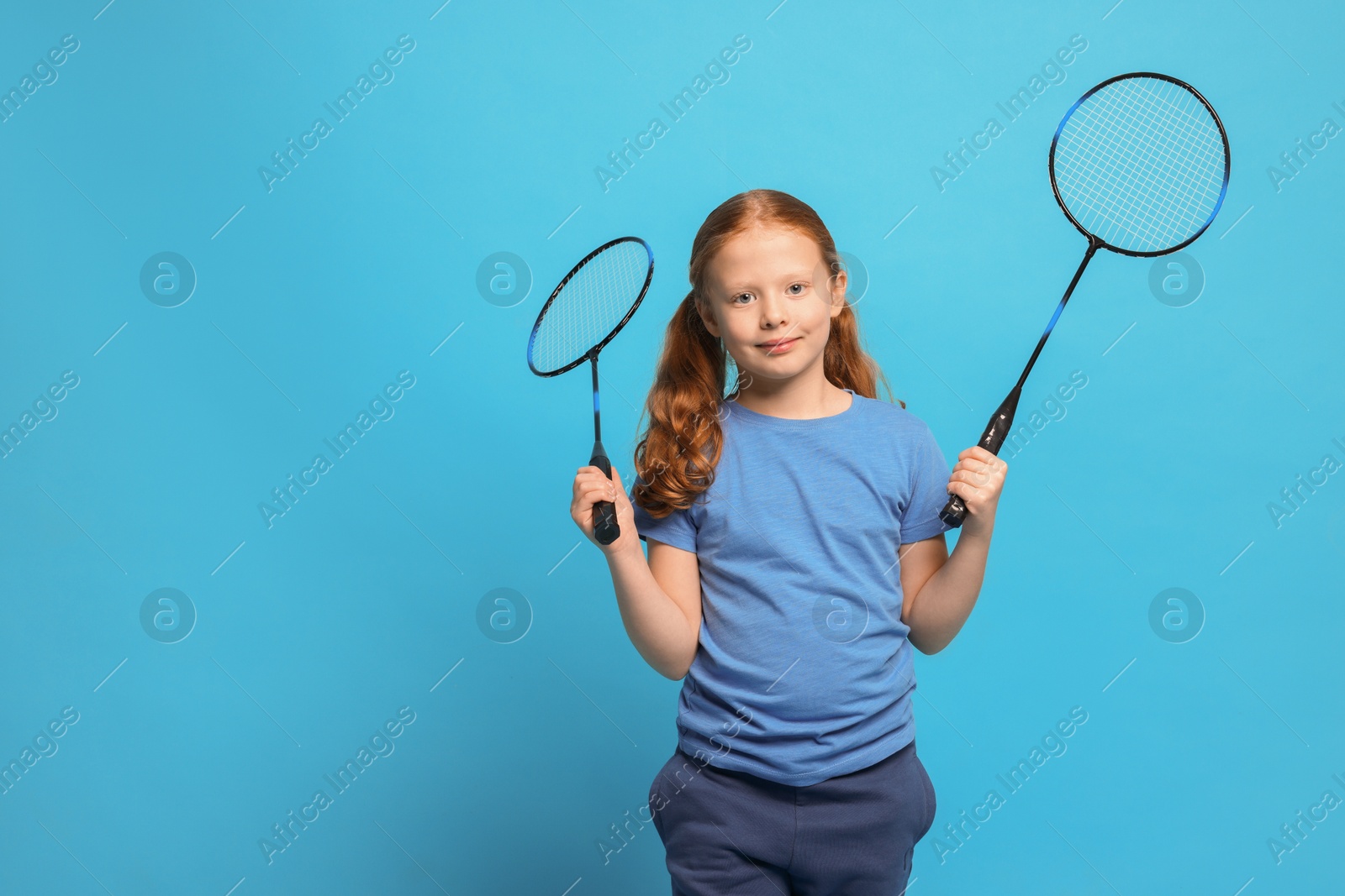 Photo of Little girl with badminton rackets on light blue background, space for text