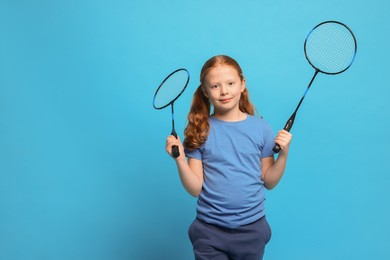 Photo of Little girl with badminton rackets on light blue background, space for text