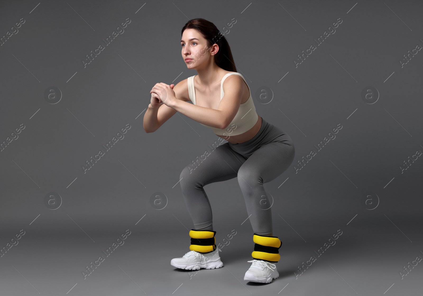 Photo of Woman in sportswear exercising with ankle weights on grey background