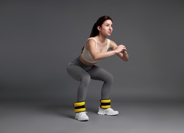 Photo of Woman in sportswear exercising with ankle weights on grey background