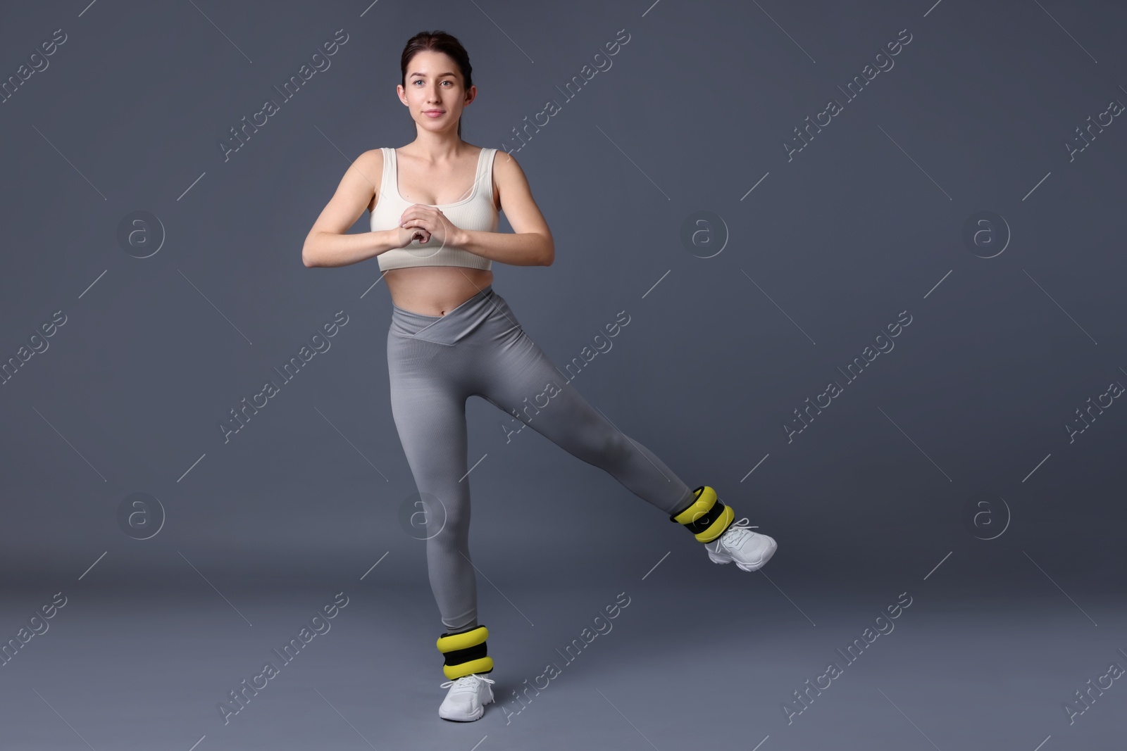 Photo of Woman in sportswear exercising with ankle weights on grey background