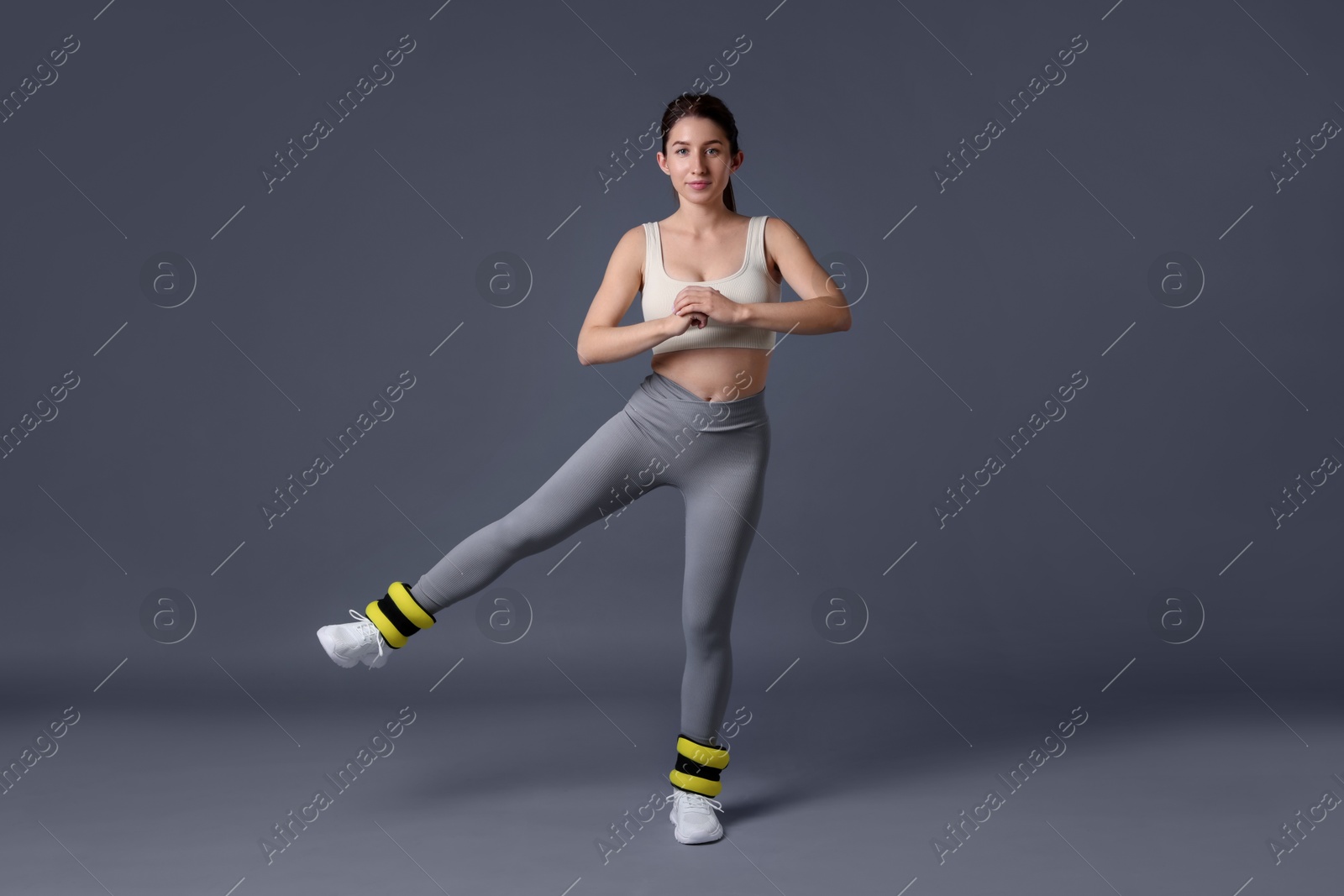 Photo of Woman in sportswear exercising with ankle weights on grey background