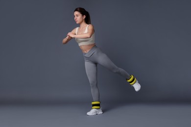 Photo of Woman in sportswear exercising with ankle weights on grey background