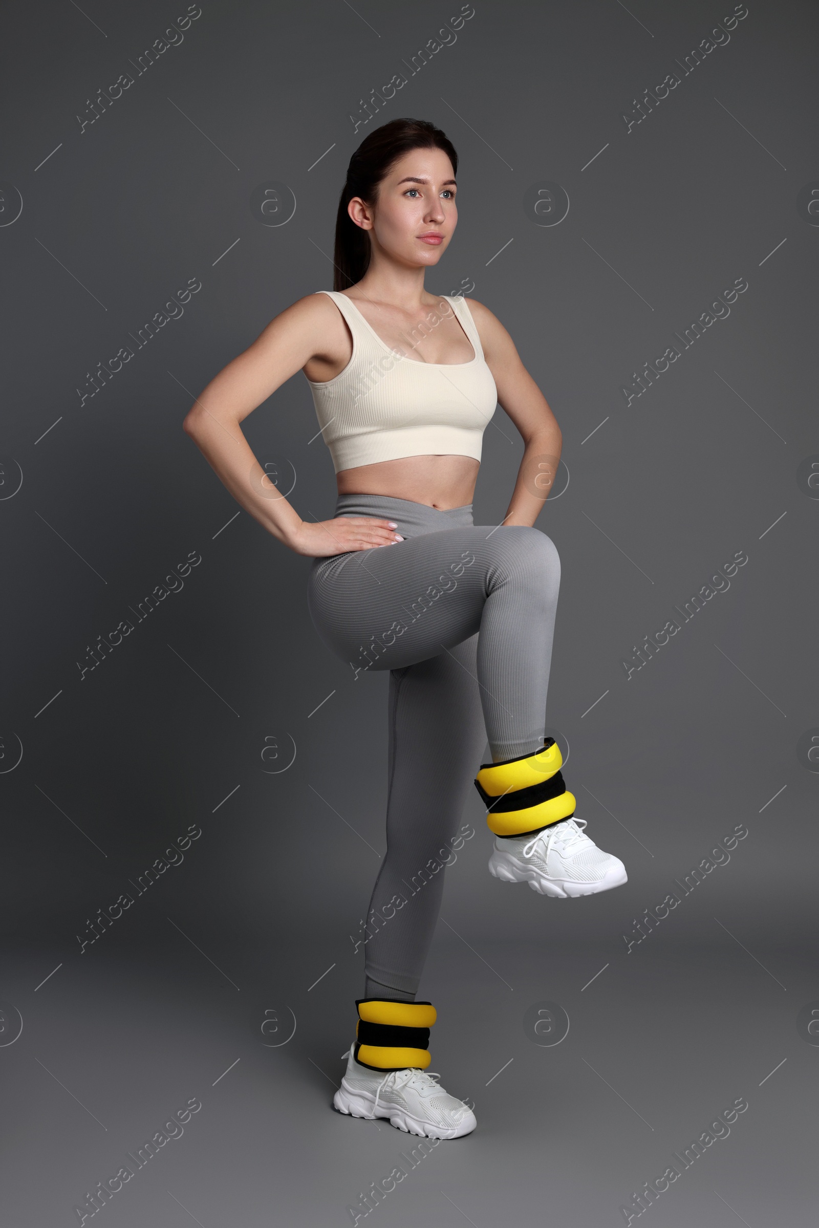 Photo of Woman in sportswear exercising with ankle weights on grey background