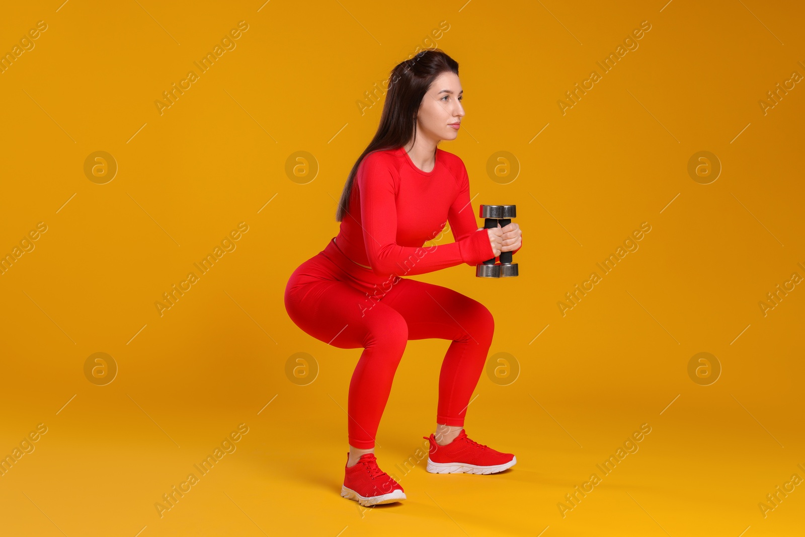 Photo of Woman in sportswear exercising with dumbbells on orange background