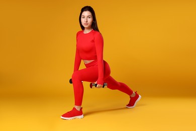 Photo of Woman in sportswear exercising with dumbbells on orange background