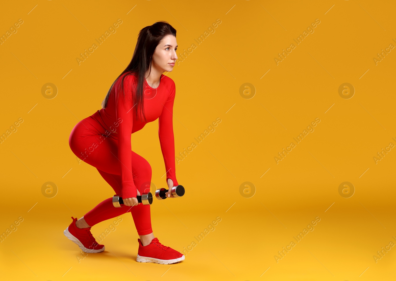 Photo of Woman in sportswear exercising with dumbbells on orange background, space for text