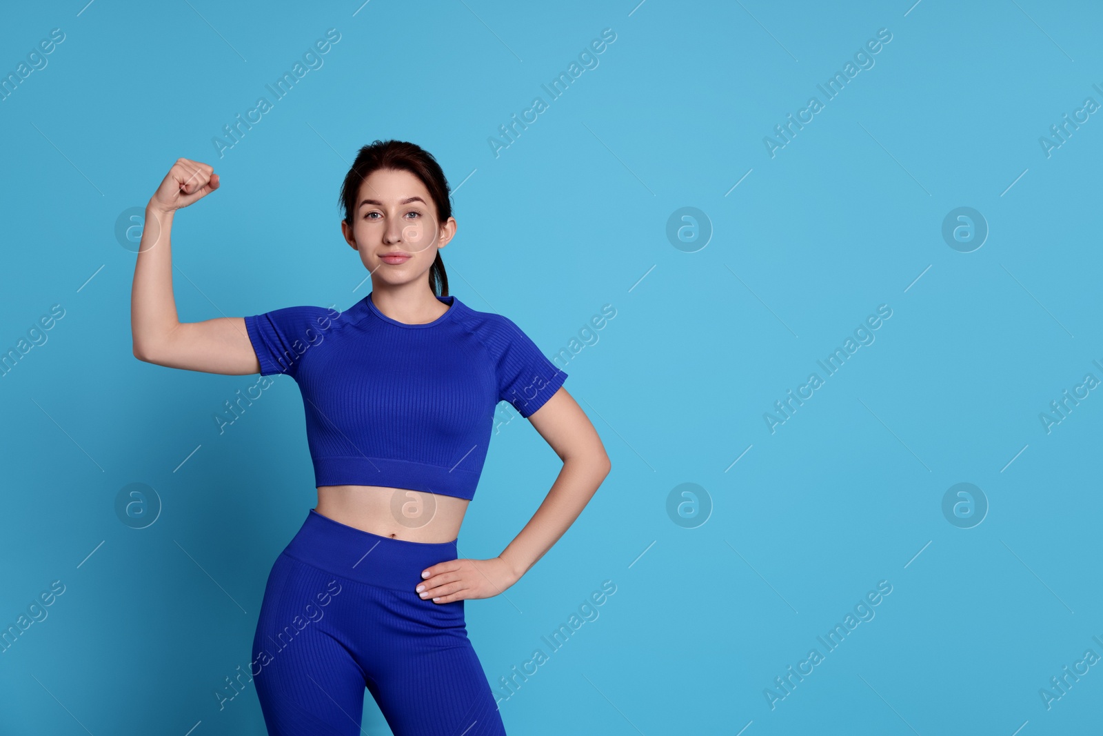 Photo of Woman in sportswear showing her bicep on light blue background, space for text