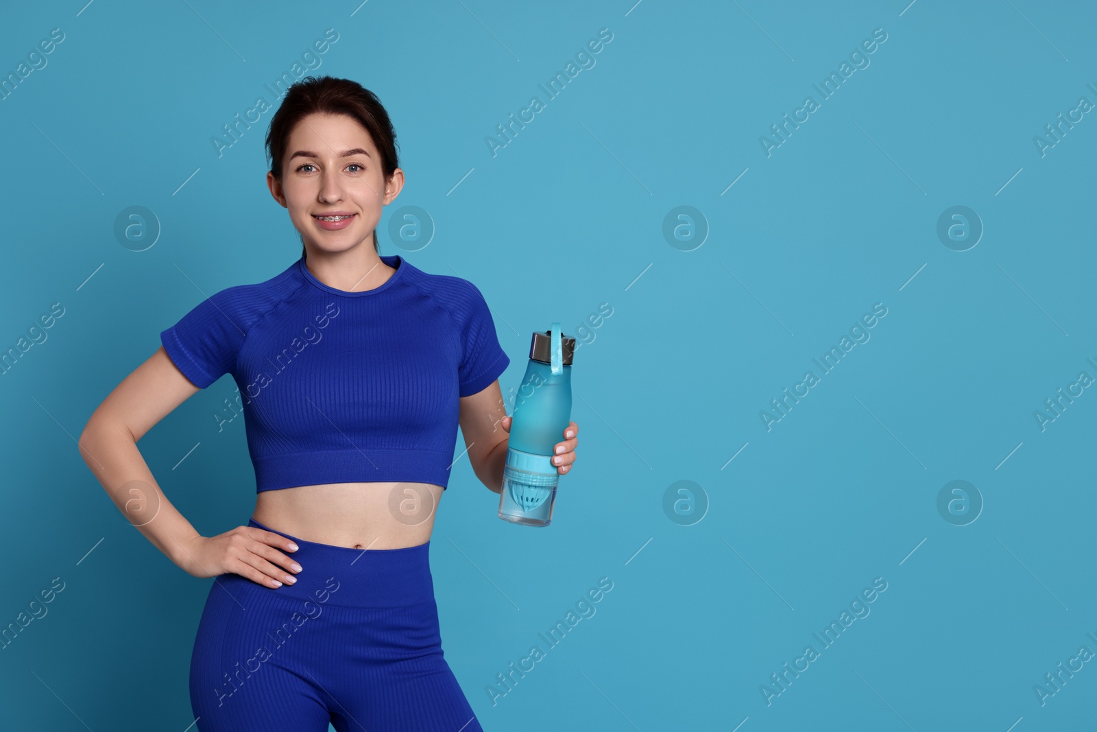 Photo of Woman in sportswear with bottle of water on light blue background, space for text