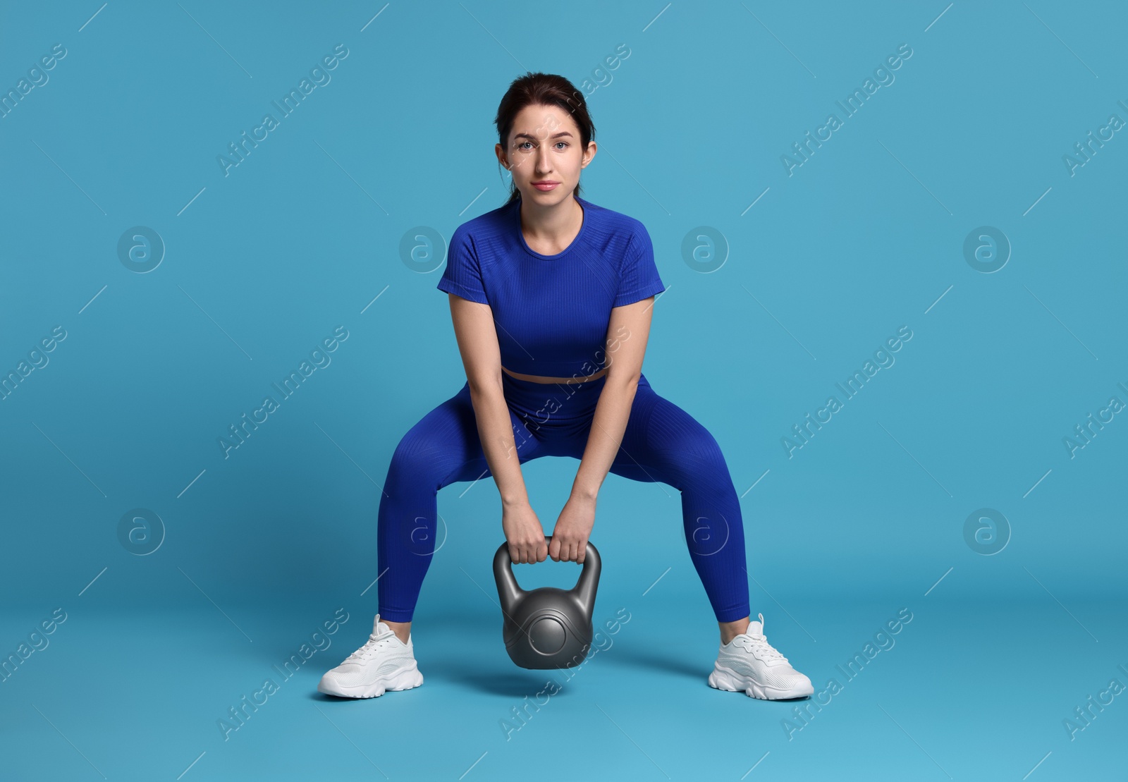 Photo of Woman in sportswear exercising with kettlebell on light blue background