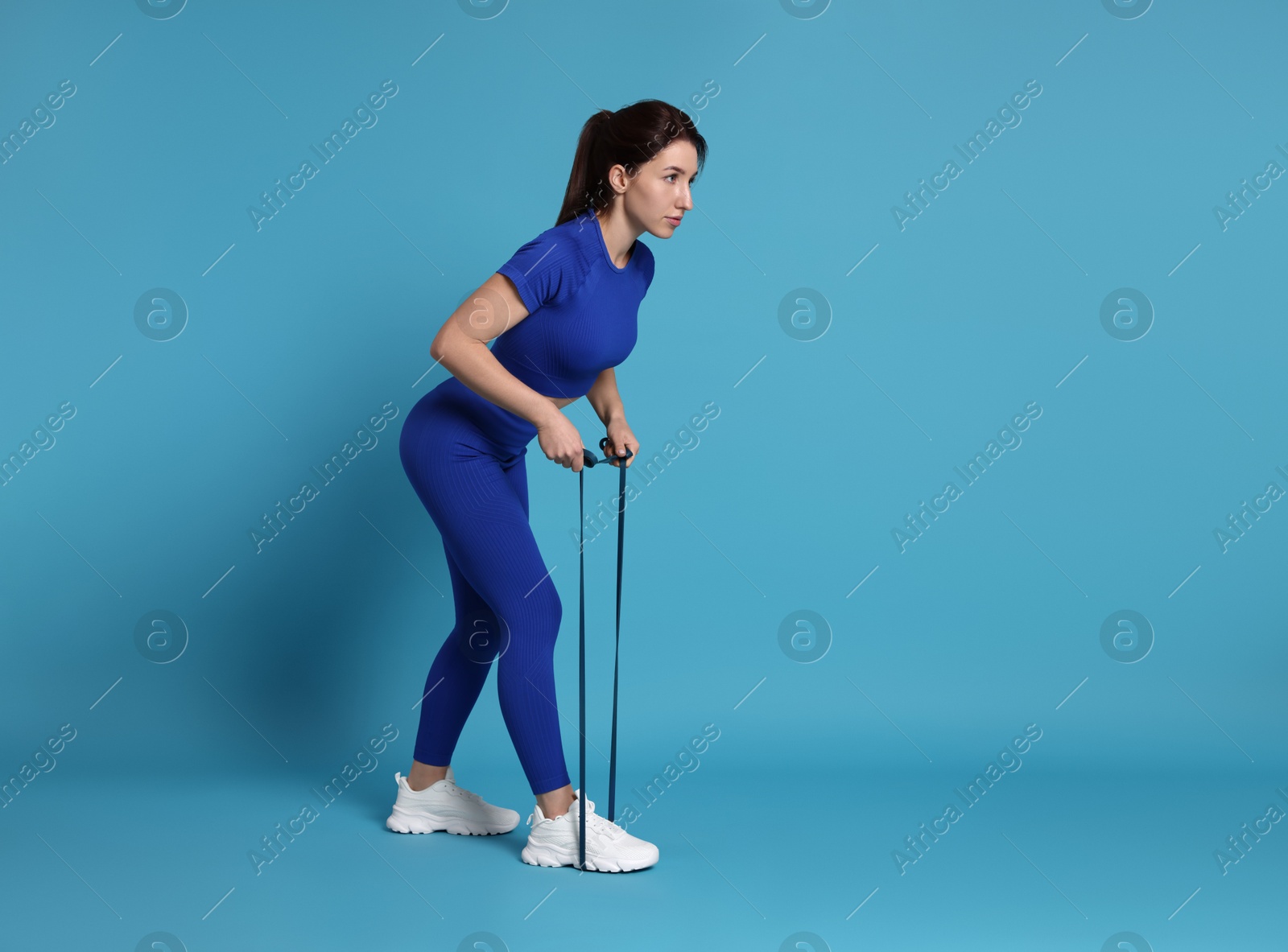 Photo of Woman in sportswear exercising elastic band on light blue background, space for text