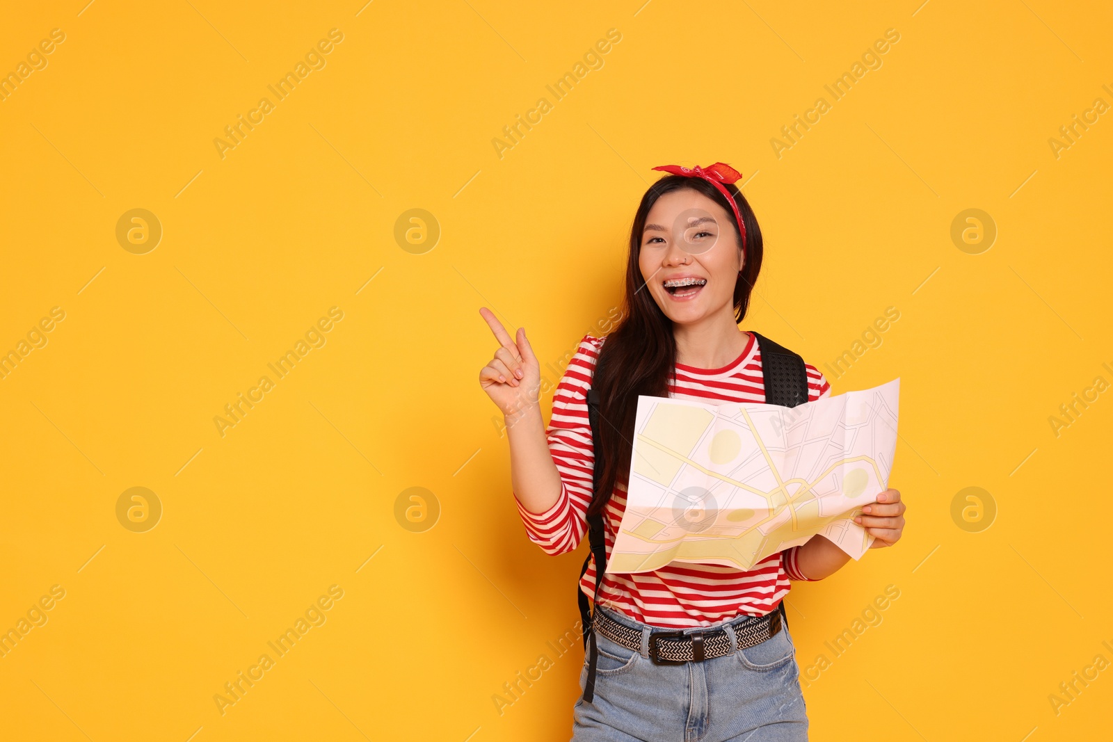 Photo of Happy traveller with map pointing at something on yellow background. Space for text