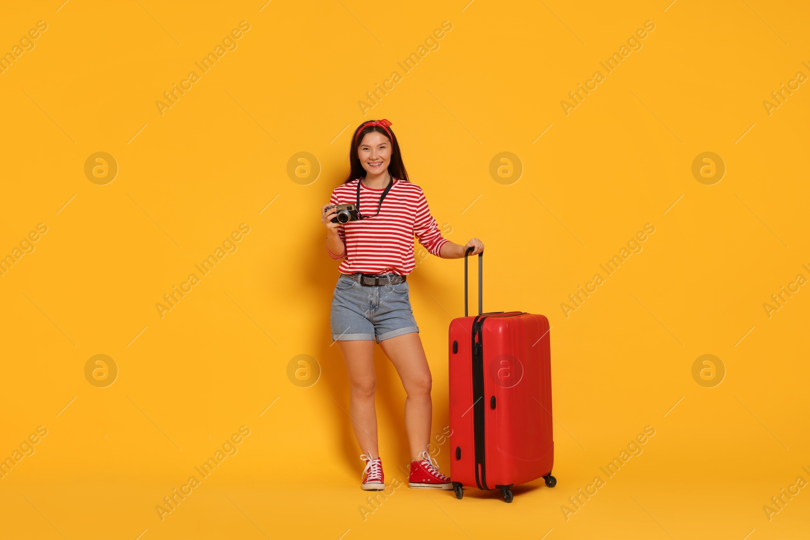 Photo of Happy traveller with camera and suitcase on yellow background