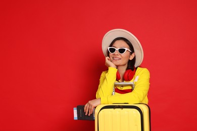 Photo of Happy traveller with headphones, passport and suitcase on red background. Space for text