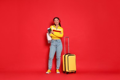 Photo of Happy traveller with passport and suitcase on red background