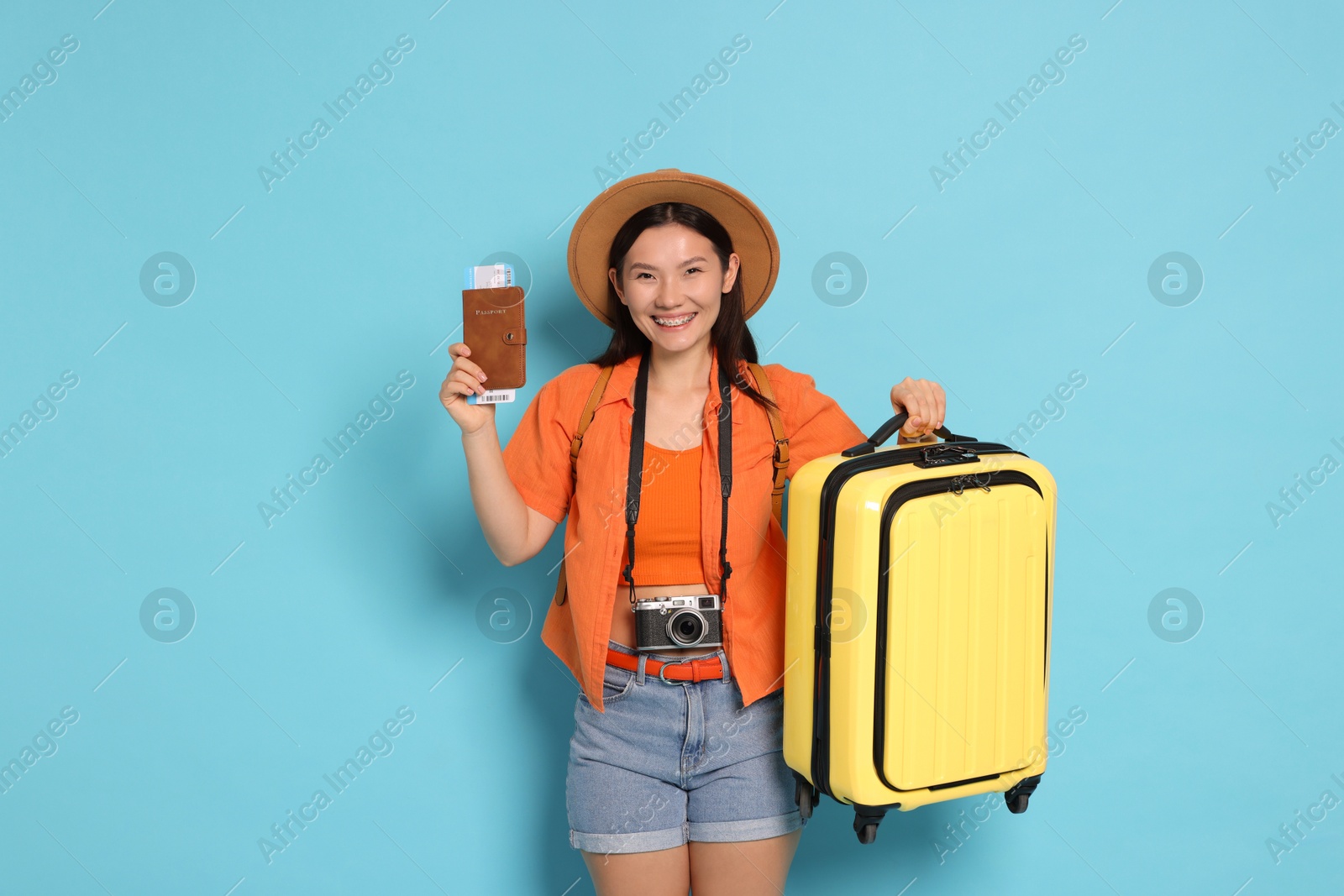 Photo of Happy traveller with passport and suitcase on light blue background