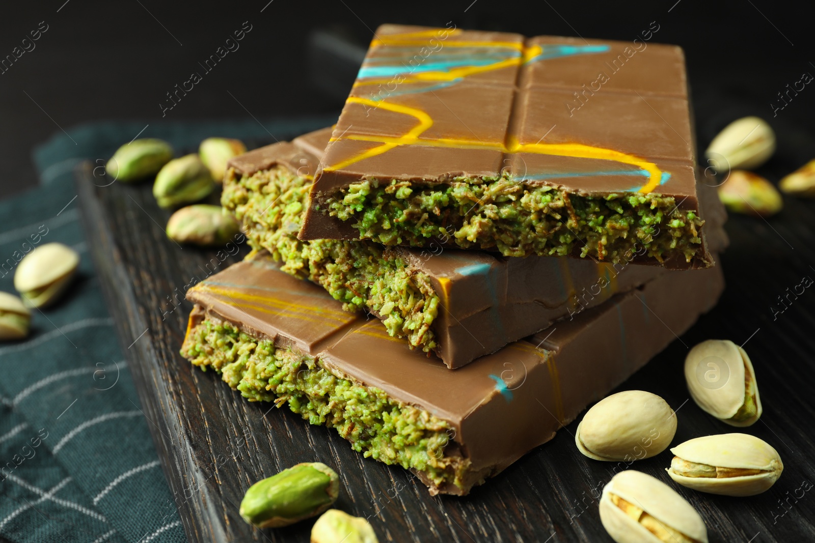 Photo of Pieces of Dubai chocolate bars with pistachios and knafeh on black table, closeup