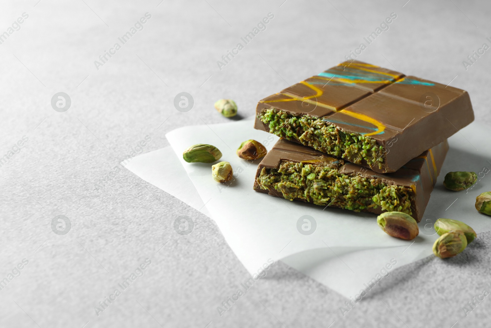 Photo of Pieces of Dubai chocolate bar with pistachios and knafeh on light grey table, closeup. Space for text