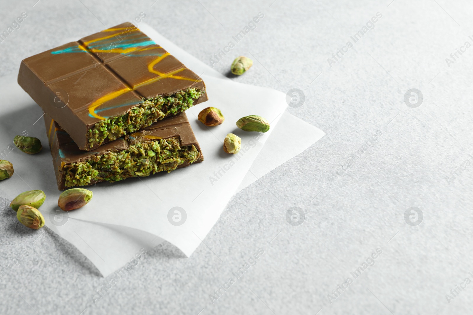 Photo of Pieces of Dubai chocolate bar with pistachios and knafeh on light grey table, closeup. Space for text