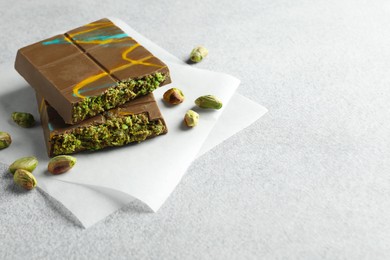 Photo of Pieces of Dubai chocolate bar with pistachios and knafeh on light grey table, closeup. Space for text