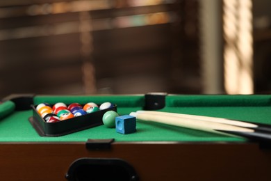 Photo of Many colorful billiard balls in triangle rack, cues and chalk on green table indoors, space for text