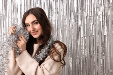 Photo of Beautiful young woman with tinsel against silver foil curtain. Space for text