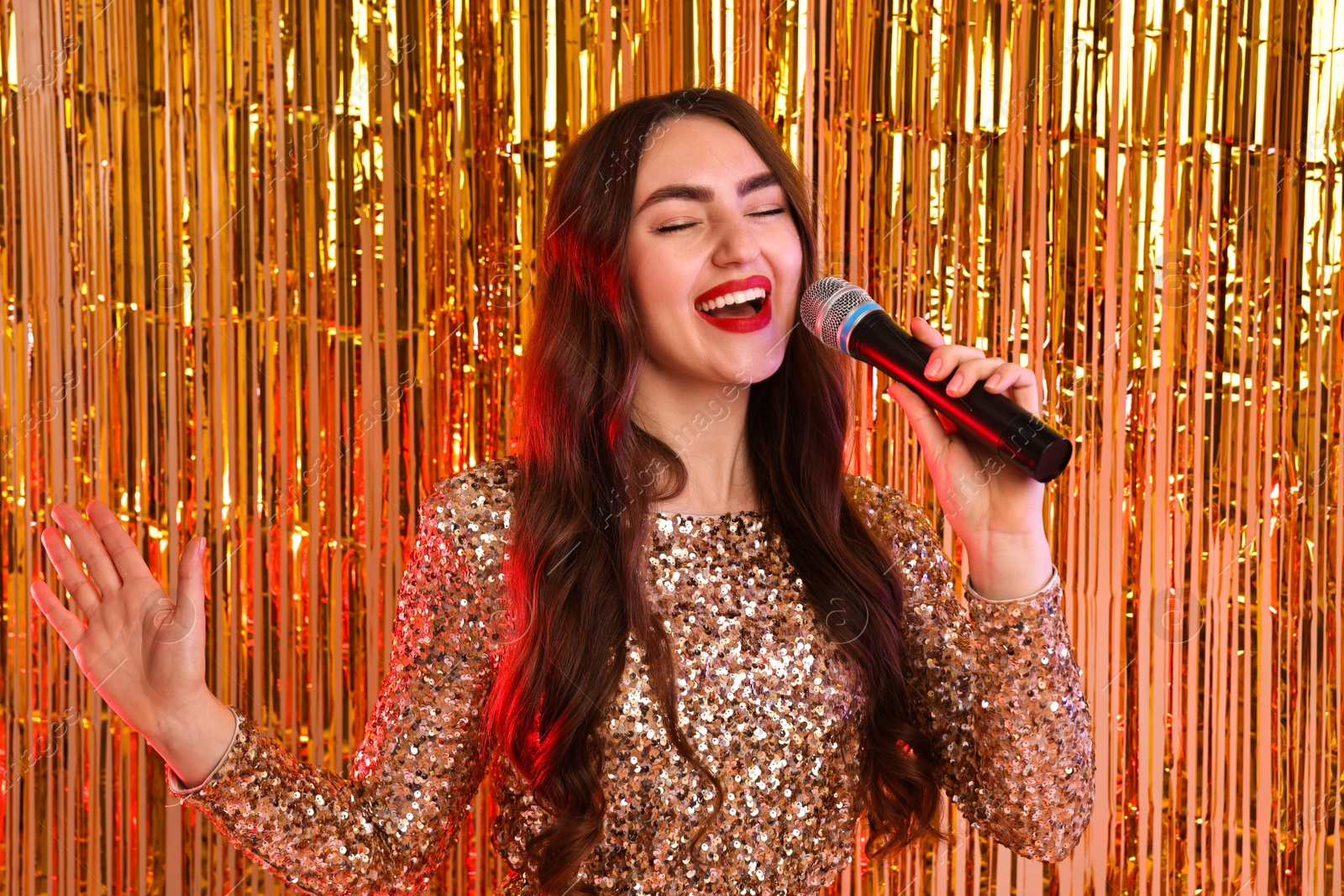 Photo of Young woman with microphone singing against foil curtain